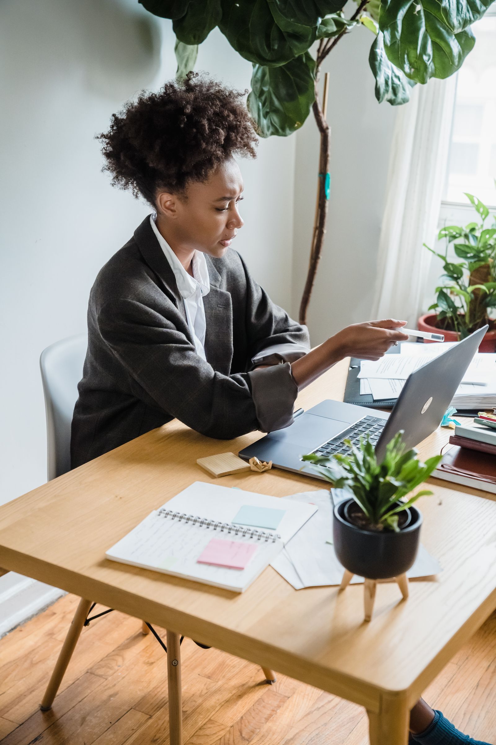 Professional working at a home desk with a laptop, notebook and plants